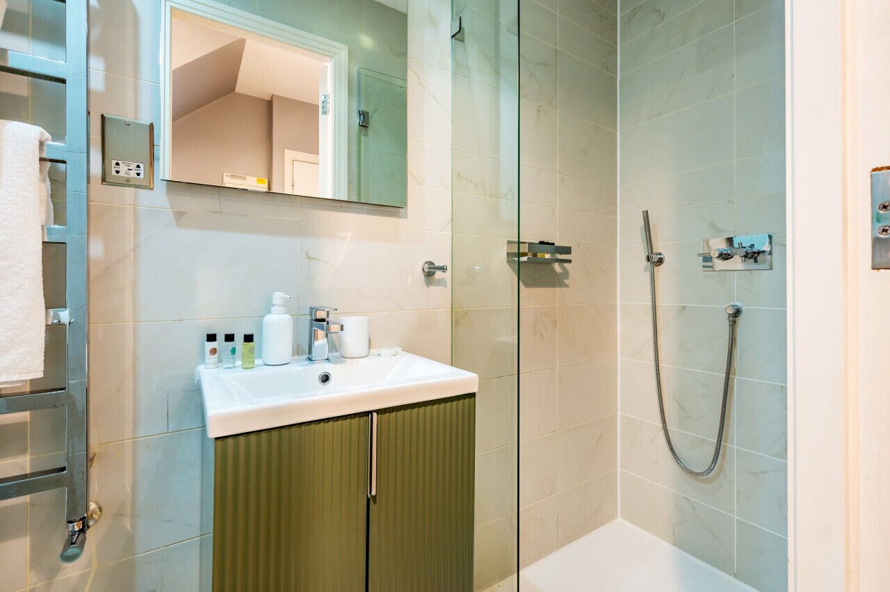 Un bagno moderno con doccia vetrata, lavandino bianco e mobili verdi, e uno specchio sopra il lavandino.