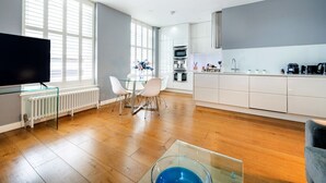 Une cuisine moderne avec des meubles blancs, un coin repas doté d’une table en verre et une grande fenêtre laissant entrer la lumière naturelle.