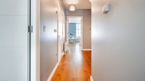 Un couloir doté d’un plancher en bois, de murs blancs et d’un luminaire au plafond.