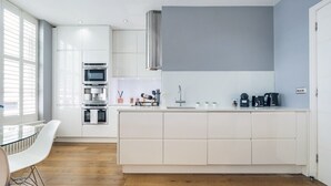 Une cuisine moderne avec des meubles blancs, une hotte en acier inoxydable et un four encastré.