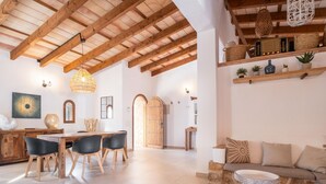 Un vaste espace de vie doté d’un plafond en bois, d’une table à manger avec des chaises, d’une cheminée en pierre et d’un coin salon confortable agrémenté de coussins.