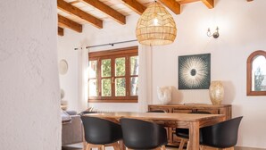 Un coin repas avec une table en bois et des chaises noires, un luminaire suspendu en fibres tressées et un appliques murales.