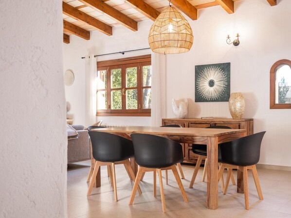 Un coin repas avec une table en bois et des chaises noires, un luminaire suspendu en fibres tressées et un appliques murales.