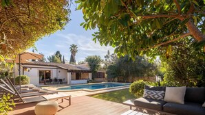 Un espace aménagé au bord de la piscine, avec une terrasse en bois, un canapé et un coin repas doté de mobilier d’extérieur.