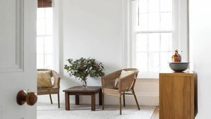 A room with a white door, a wicker chair, a small table with a vase, and a wooden cabinet.