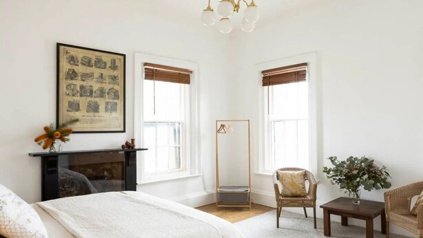 A bedroom with a bed, a chair, a small table, a mirror, and a fireplace.