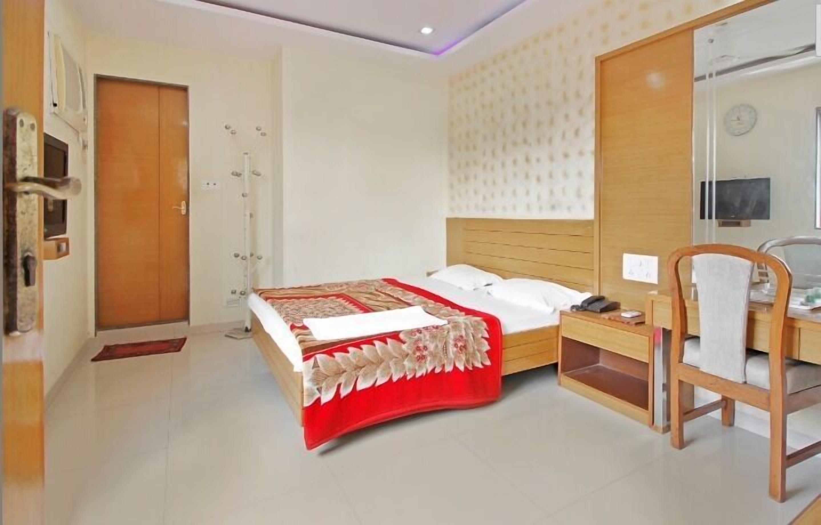 A hotel room with a bed, bedside table, chair, and a mirror.