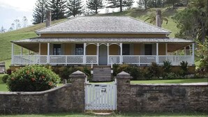 A two-story house with a porch, stone walls, and a gate.