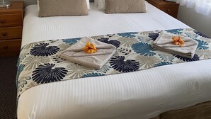 A neatly made bed with a floral bedspread, two nightstands with lamps, a framed picture on the wall, and a window with sheer curtains.
