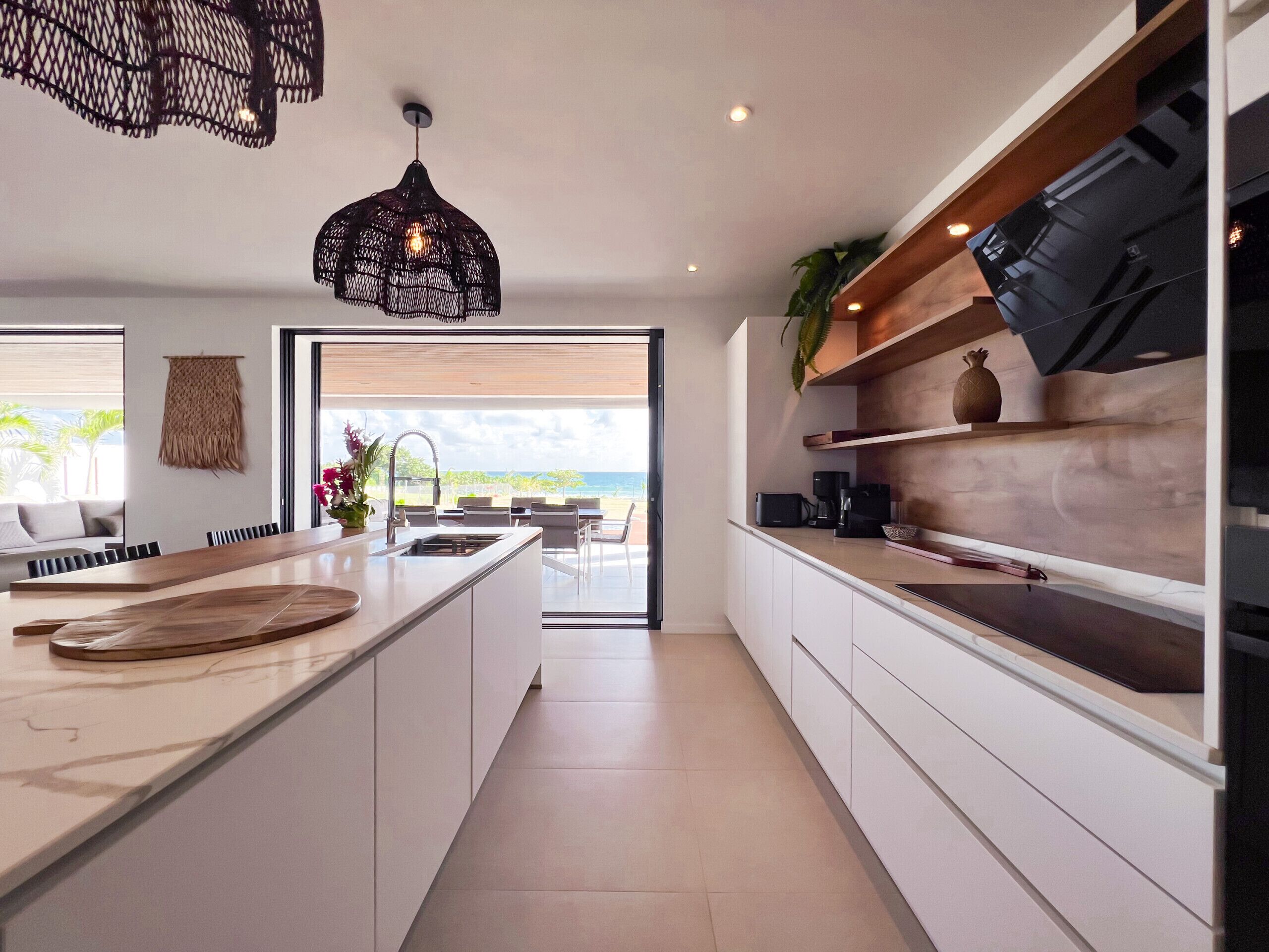 Een moderne keuken met een groot eiland, witte kastjes en uitzicht op de oceaan.