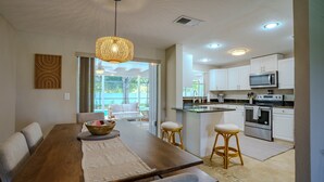 A modern kitchen with white cabinets, a microwave, and an oven. There is a dining area with a wooden table and chairs. - 2BR Retreat - Private Pool Near Siesta Key (Sarasota)