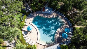 Une vue aérienne d’une piscine entourée de chaises longues et de parasols, avec des palmiers et un petit bâtiment à proximité.