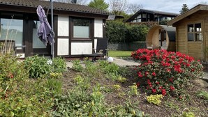 Een houten chalet met een klein terras en een tuin vol planten en bloemen.