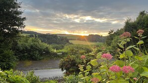 Een weelderig landschap met een rivier, dichte begroeiing en een zonsondergang op de achtergrond.
