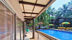 A poolside area with a clear view of the pool, a covered seating area, and a building with outdoor seating. - Beach Walk Resort - Goa (Morjim)