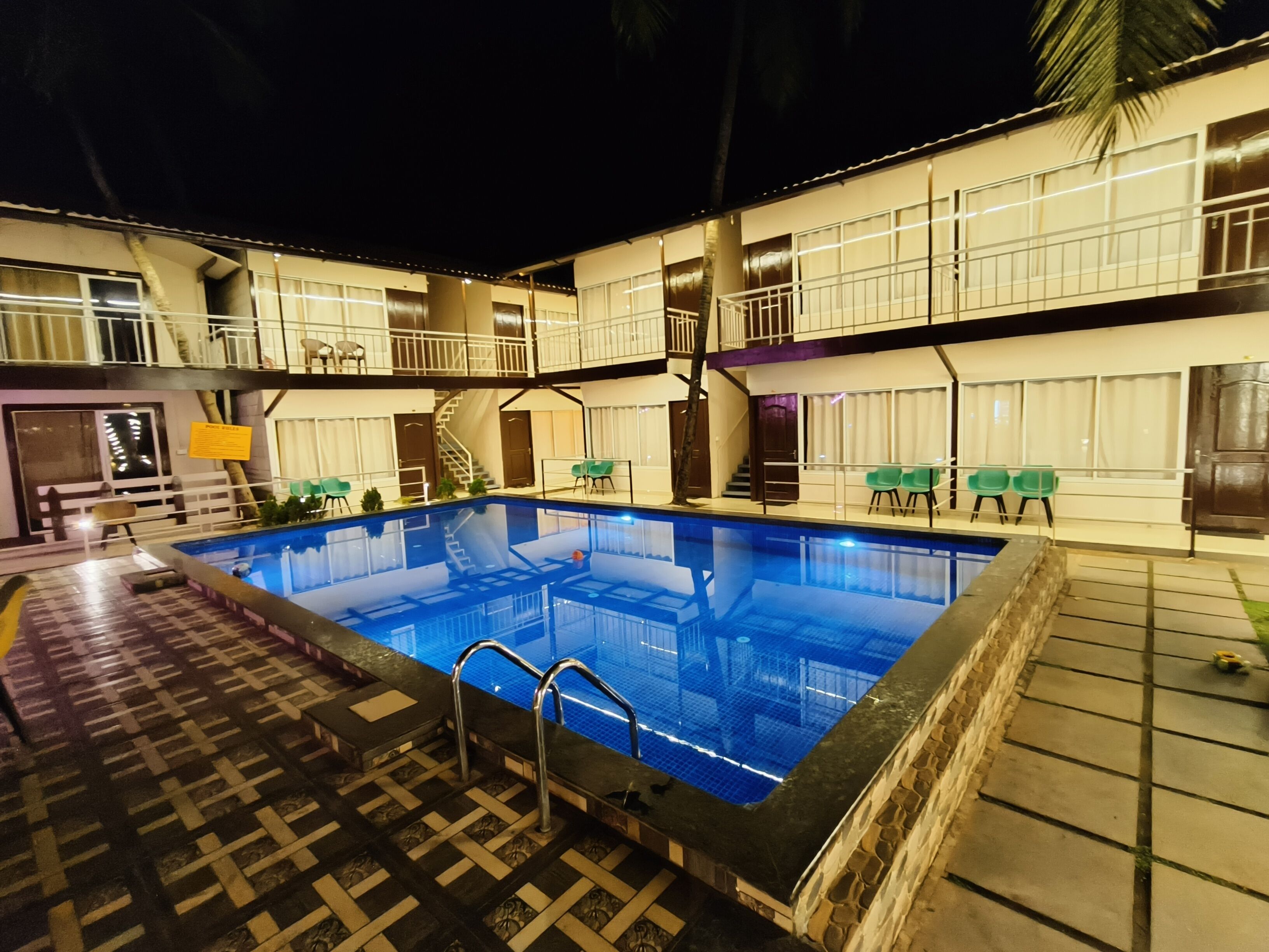 Una piscina con borde de baldosas, rodeada por un edificio de varios pisos con balcones y mobiliario exterior.