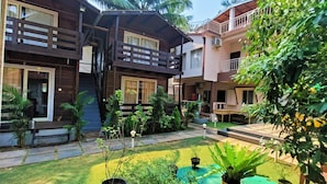 A two-story wooden house with a balcony, surrounded by potted plants and a small garden area. - Beach Walk Resort - Goa (Morjim)