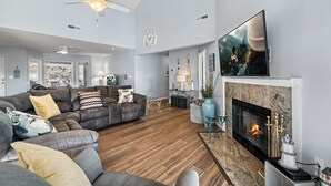 Un salon spacieux doté d’une cheminée, d’un grand téléviseur à écran plat et d’un ventilateur de plafond.