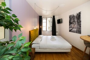 A bedroom with a bed, a wooden headboard, a bedside table, a TV on the wall, and a window with curtains.