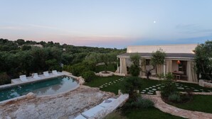 A pool with lounge chairs, a garden with a stone pathway, and a building with a covered patio. - Villa Borghetto Formica (Ostuni)