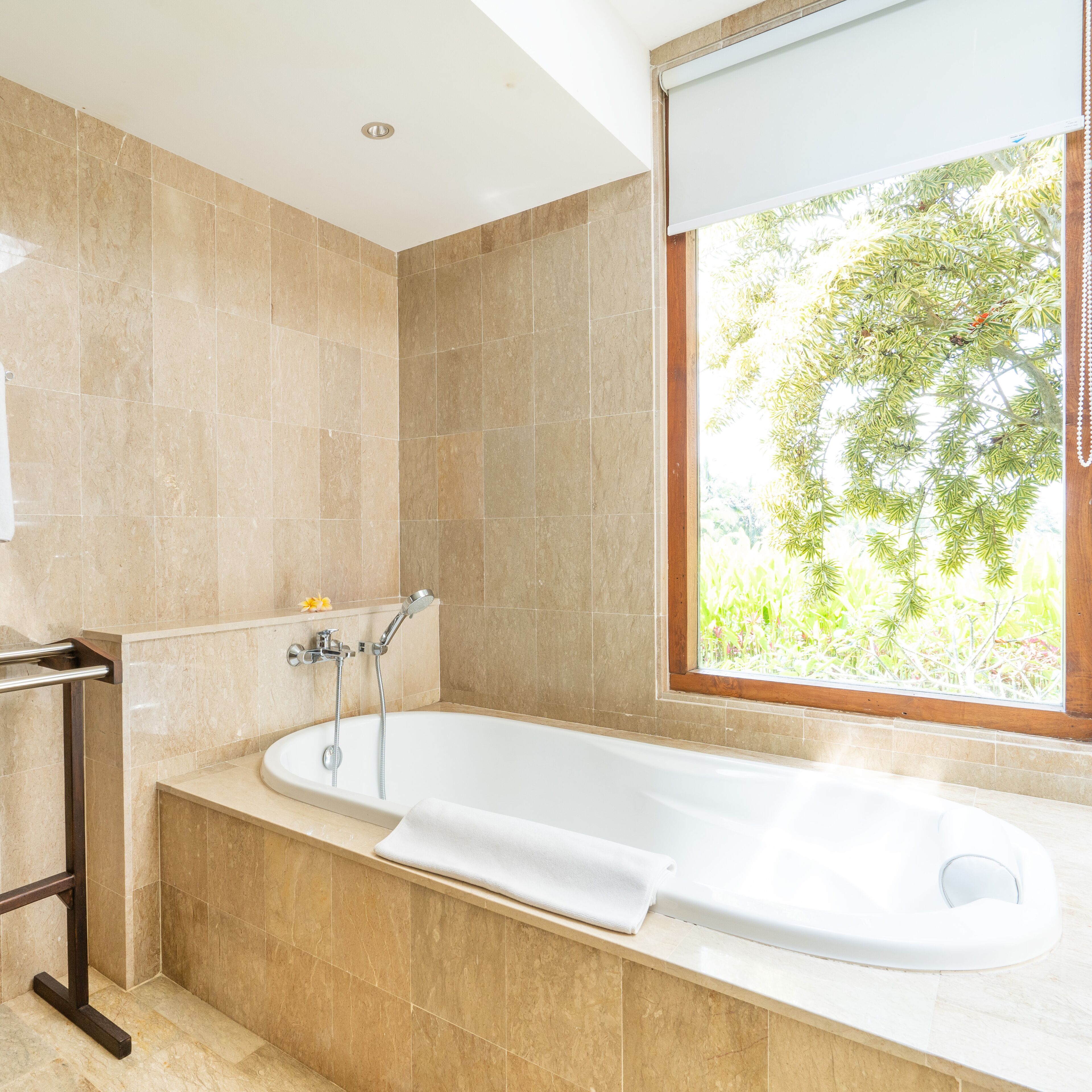 A modern bathroom with a freestanding bathtub, a window with a view of greenery, and a towel rack.
