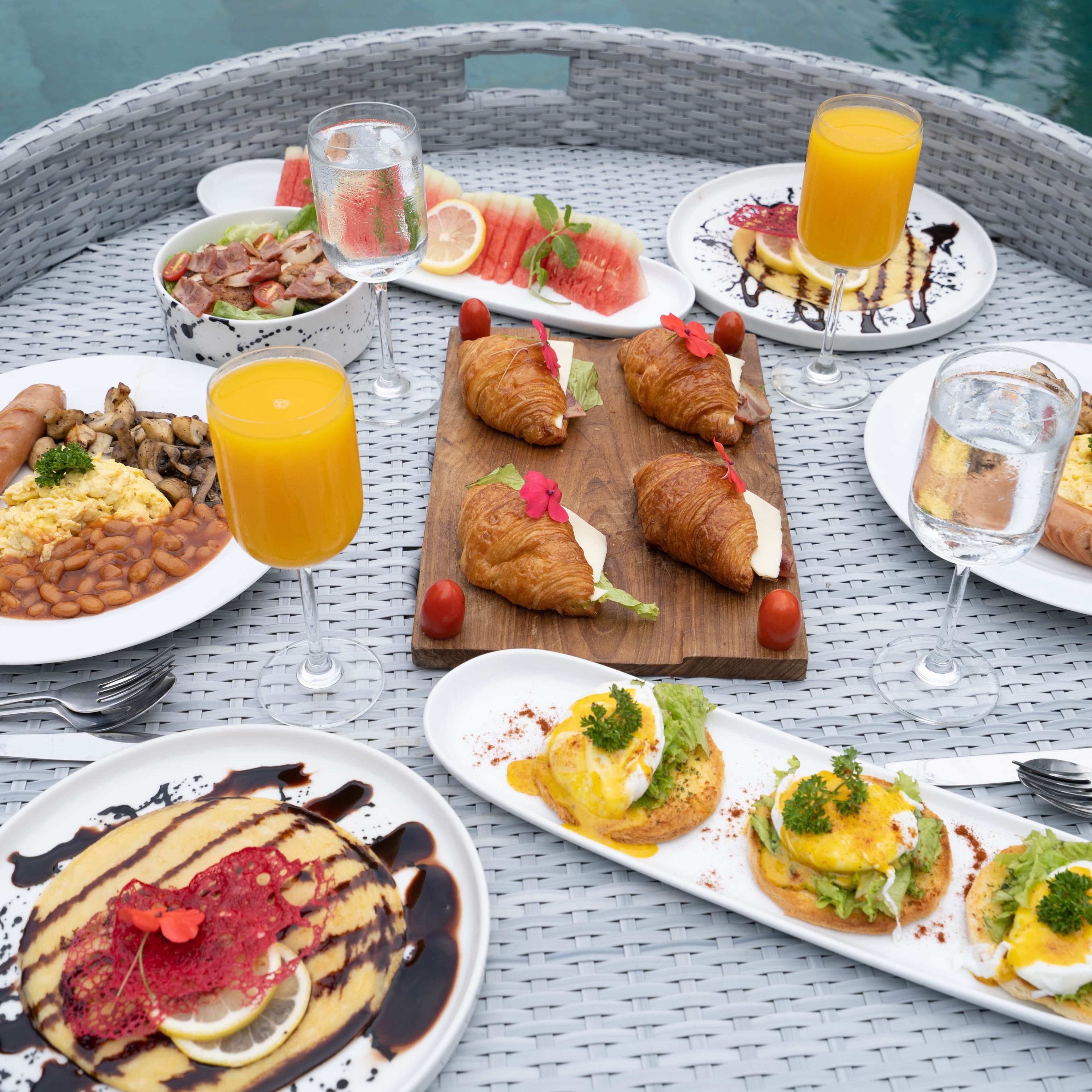 A wicker table with various breakfast items including croissants, eggs, and fruit.