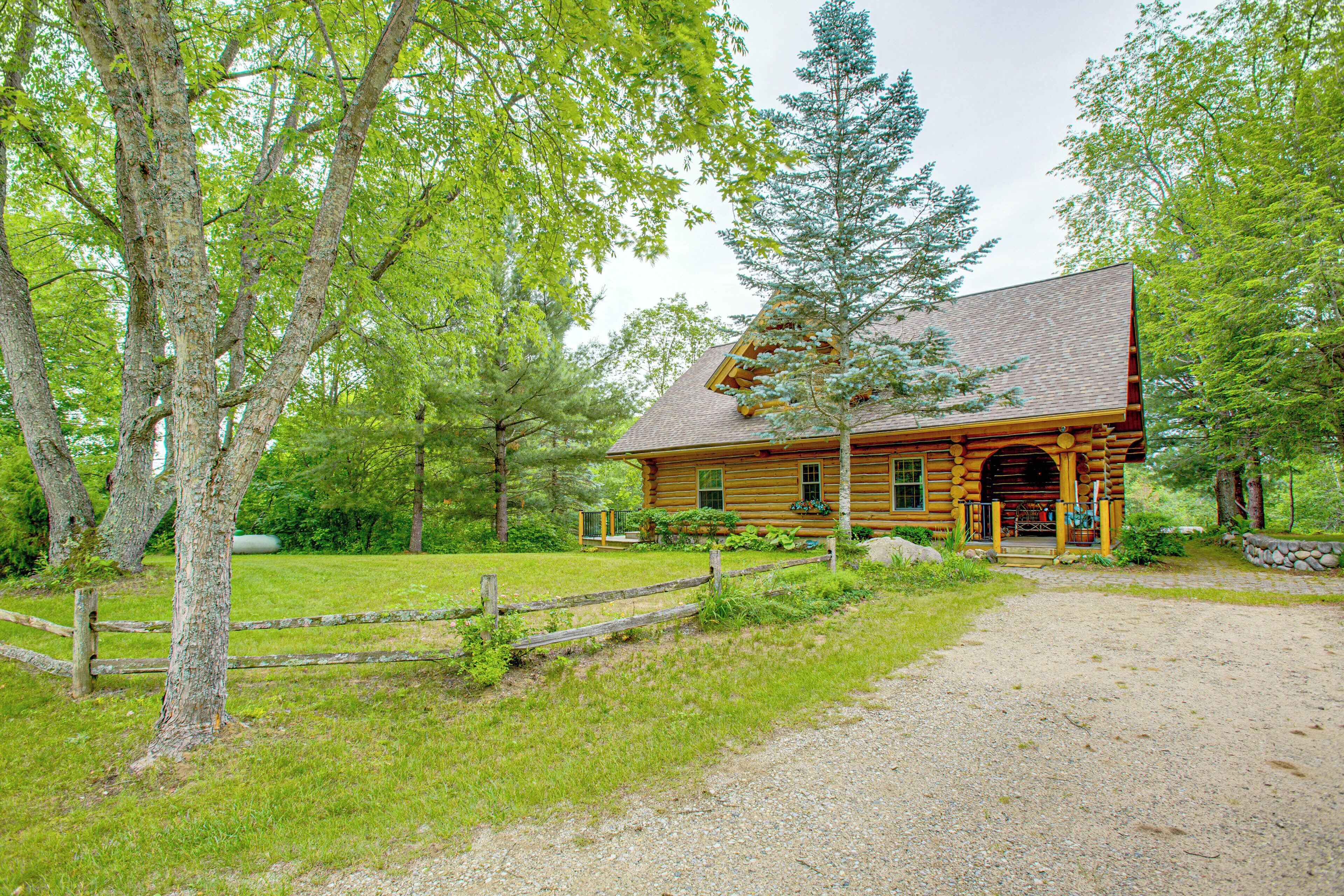 A rustic log cabin with a gravel driveway and a wooden fence.