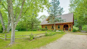 A rustic log cabin with a gravel driveway and a wooden fence.