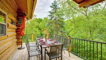 A wooden deck with a table set for dining, surrounded by chairs, overlooking a forested area.