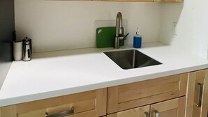 A kitchen with wooden cabinets, a white countertop, a stainless steel sink, and a green cutting board. - Comfortable lodging close to Whitewater & town (Nelson)