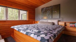 A wooden cabin bedroom with a bed, a window, and a painting on the wall. - Comfortable lodging close to Whitewater & town (Nelson)