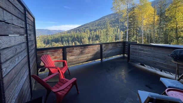 A wooden deck with red Adirondack chairs, overlooking a forested mountain range. - Comfortable lodging close to Whitewater & town (Nelson)