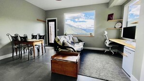 A modern room with a dining area, a sofa, a desk with a computer, and a large window with a mountain view. - Comfortable lodging close to Whitewater & town (Nelson)