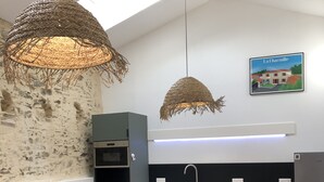 A modern kitchen with a dining area, featuring a stone wall, wooden ceiling beams, and a hanging light fixture.