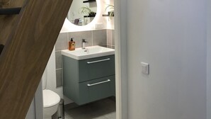 A modern bathroom with a wooden staircase, a white sink, a toilet, and a mirror with a circular light.