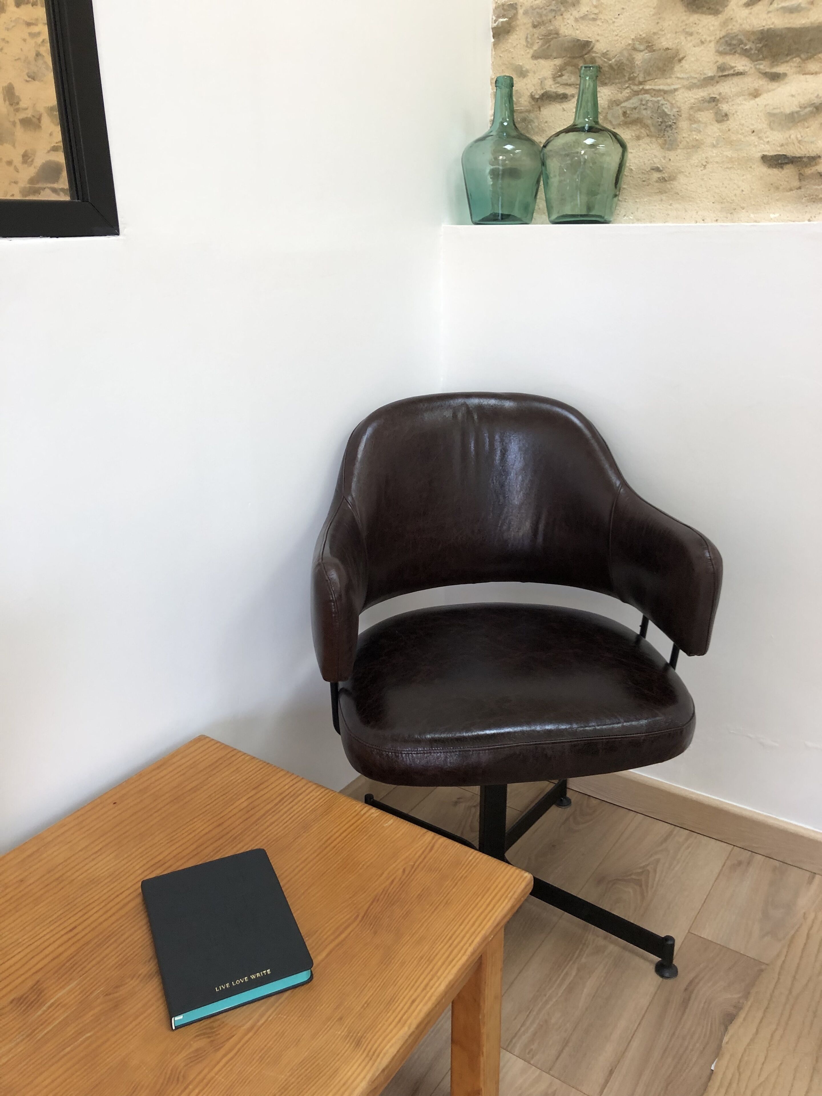 A brown leather chair next to a wooden table with a black notebook.