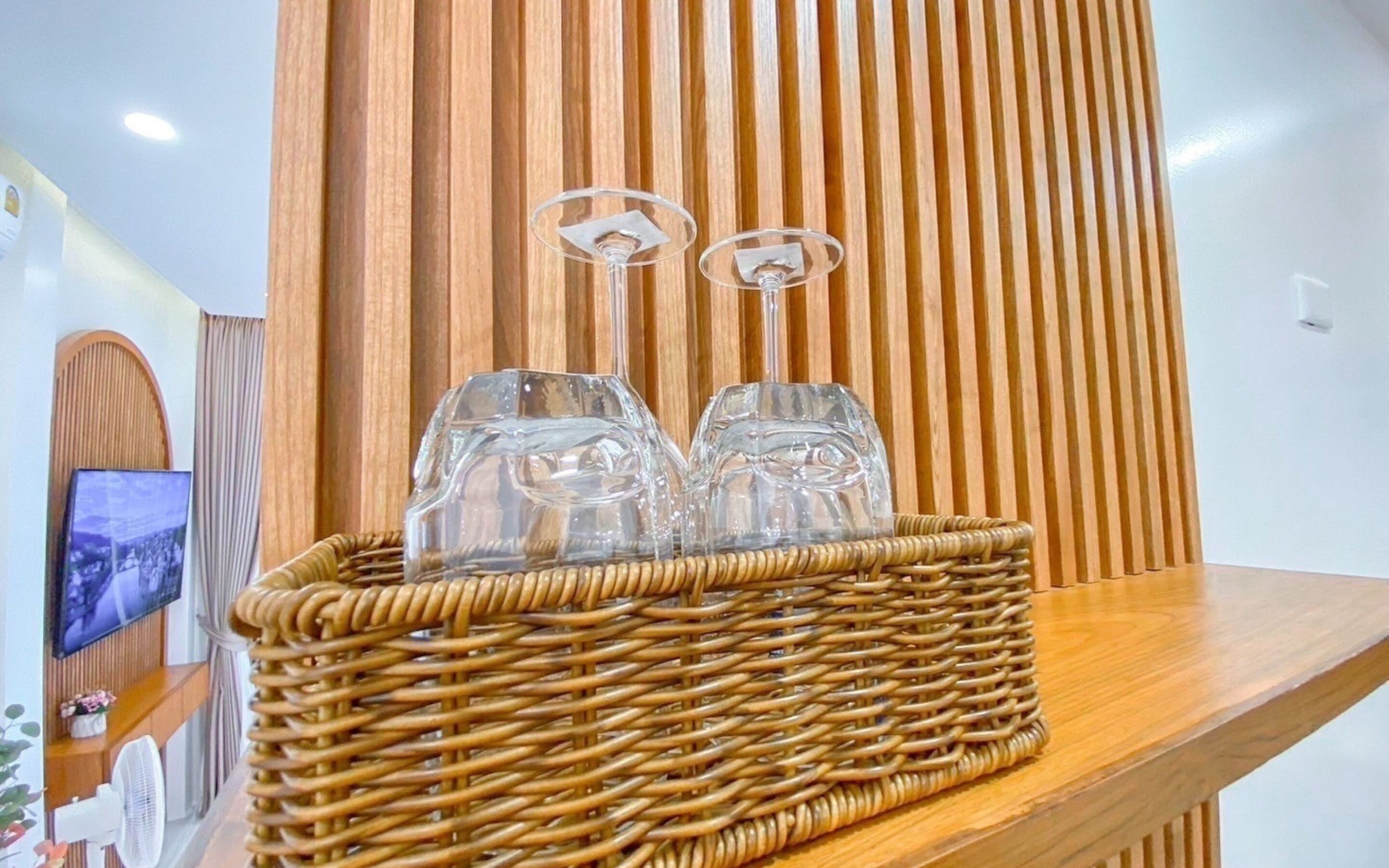 Een rieten mand met twee glazen wijnglazen op een houten plank, voor een verticale houten wand.
