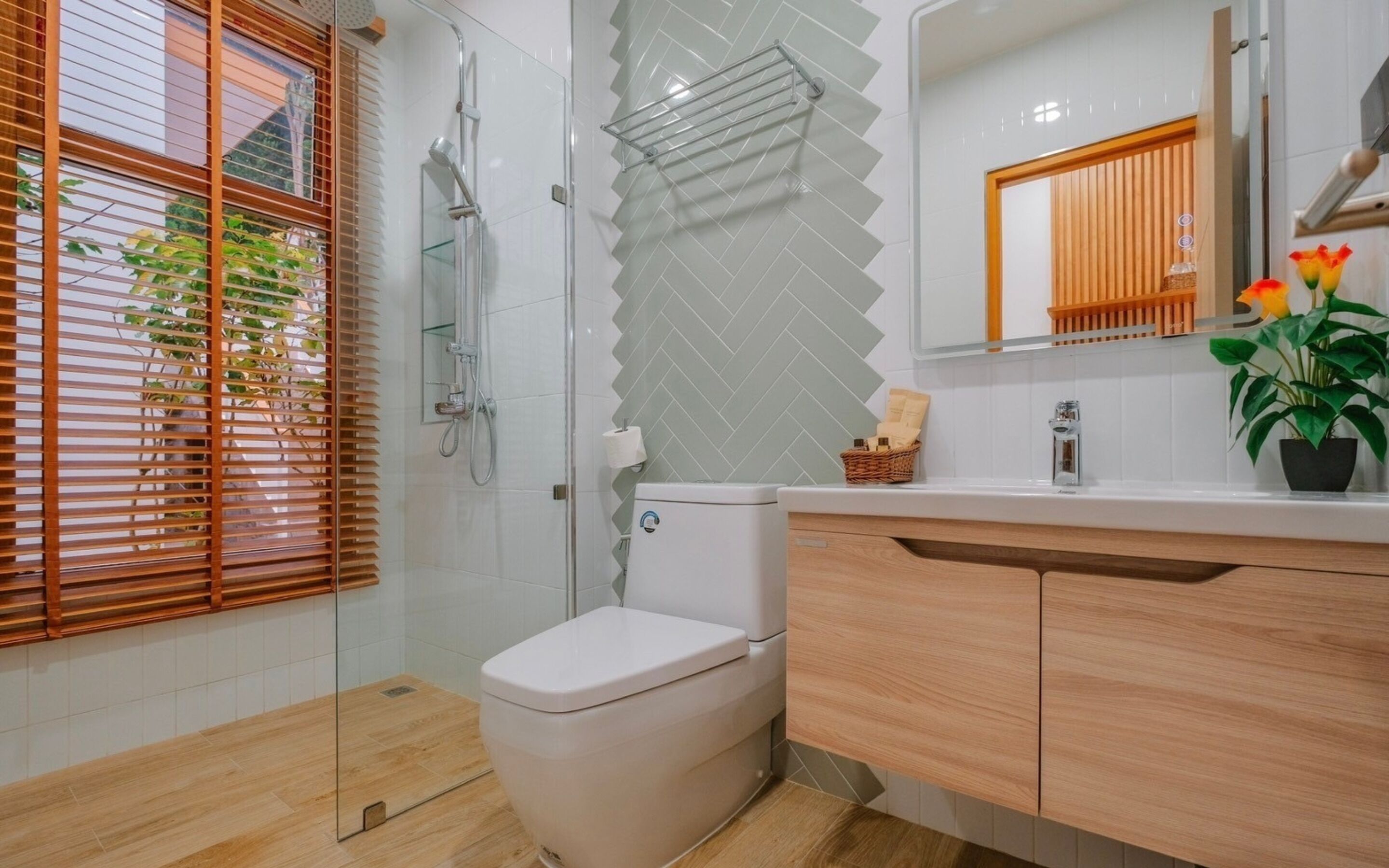 A modern bathroom with a glass shower enclosure, a toilet, a wooden vanity, and a potted plant.