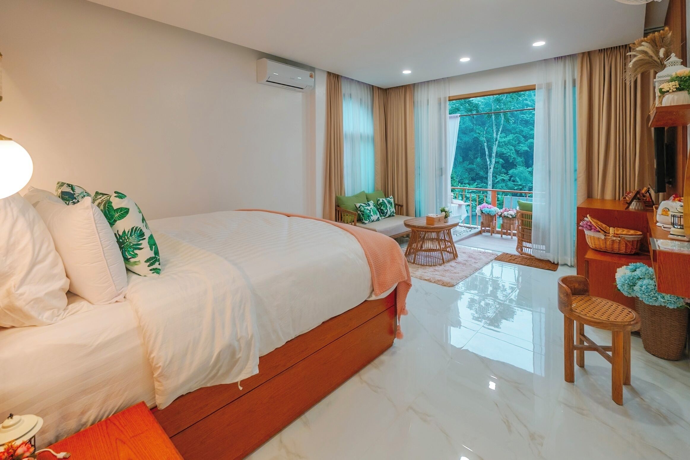 Un'ampia camera da letto con un letto grande, un balcone con vista e un'area pranzo con mobili in vimini.
