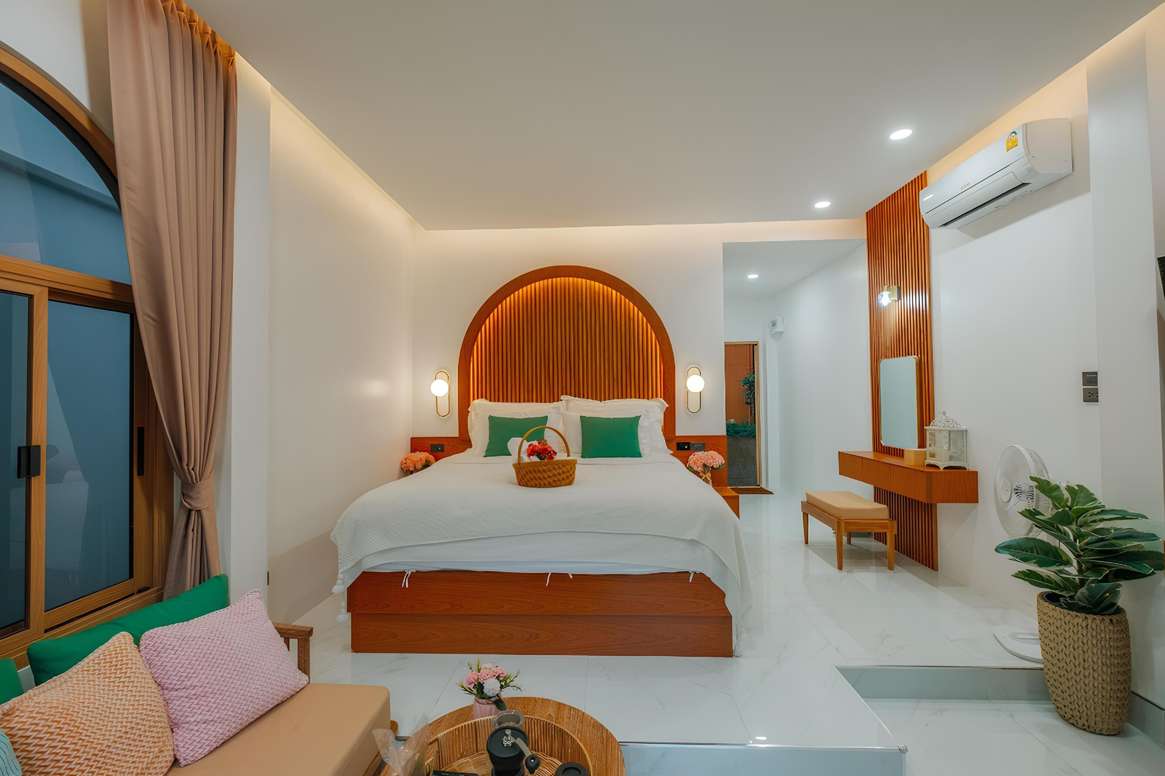 A modern hotel room with a large bed, a wooden headboard, a bedside table, a nightstand, a small bench, a potted plant, and a large mirror.