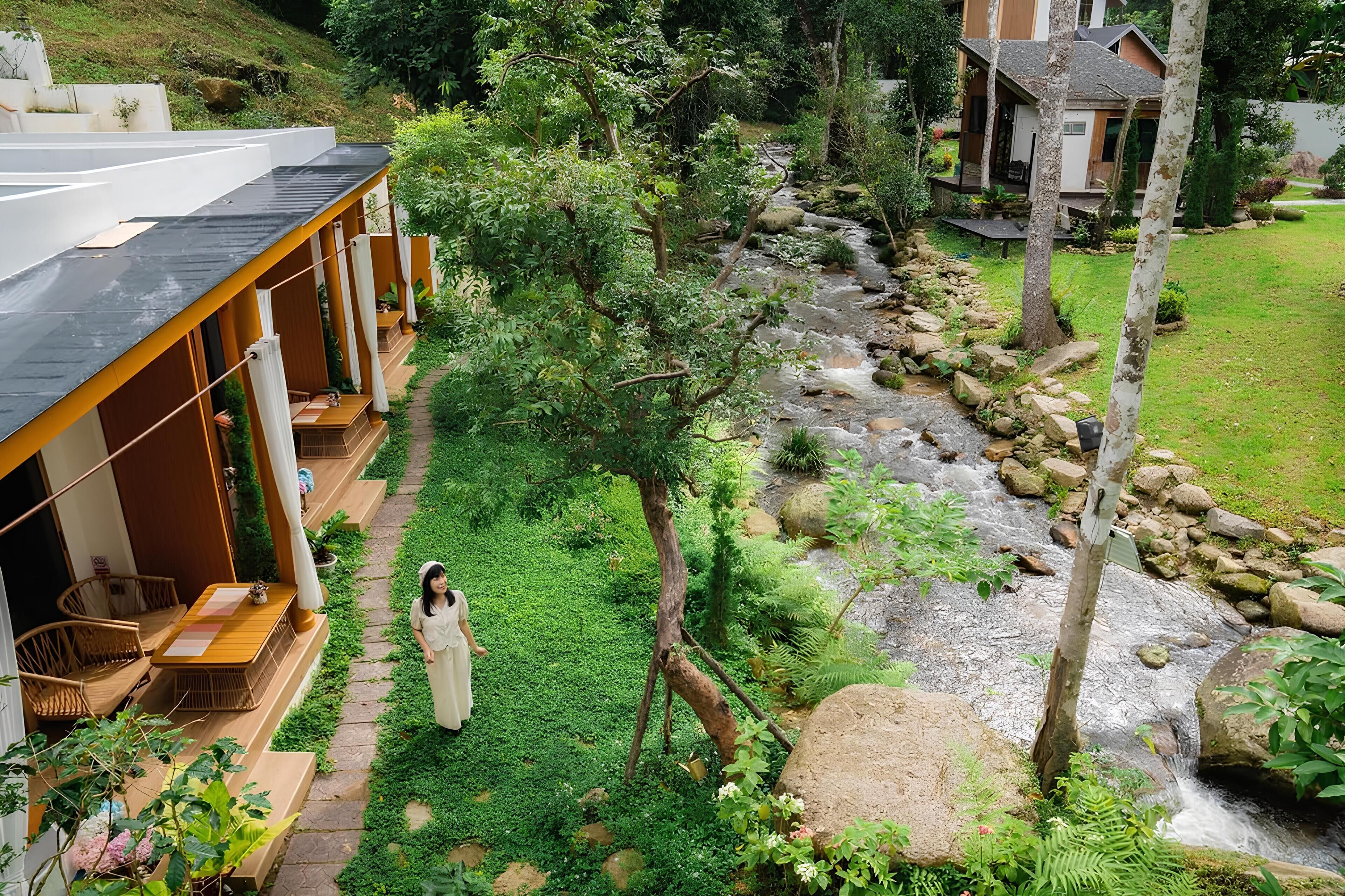 A serene garden with a stream, wooden deck, and outdoor seating area.