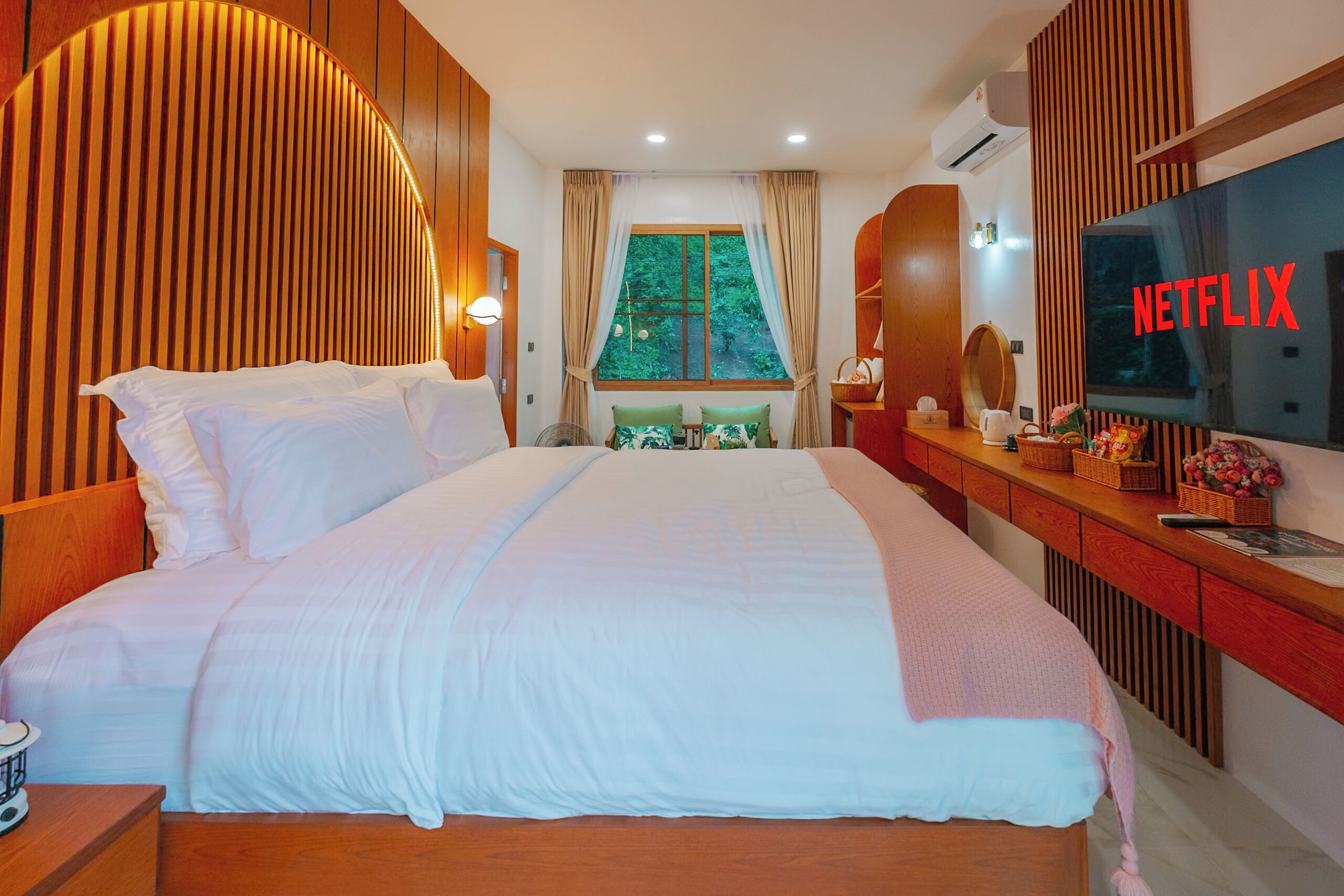 A hotel room with a large bed, a TV, a window with curtains, and a wooden headboard.