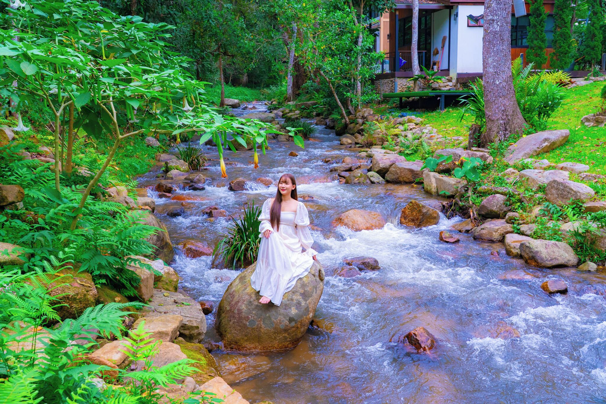 A woman sitting on a rock in a flowing river surrounded by lush greenery.