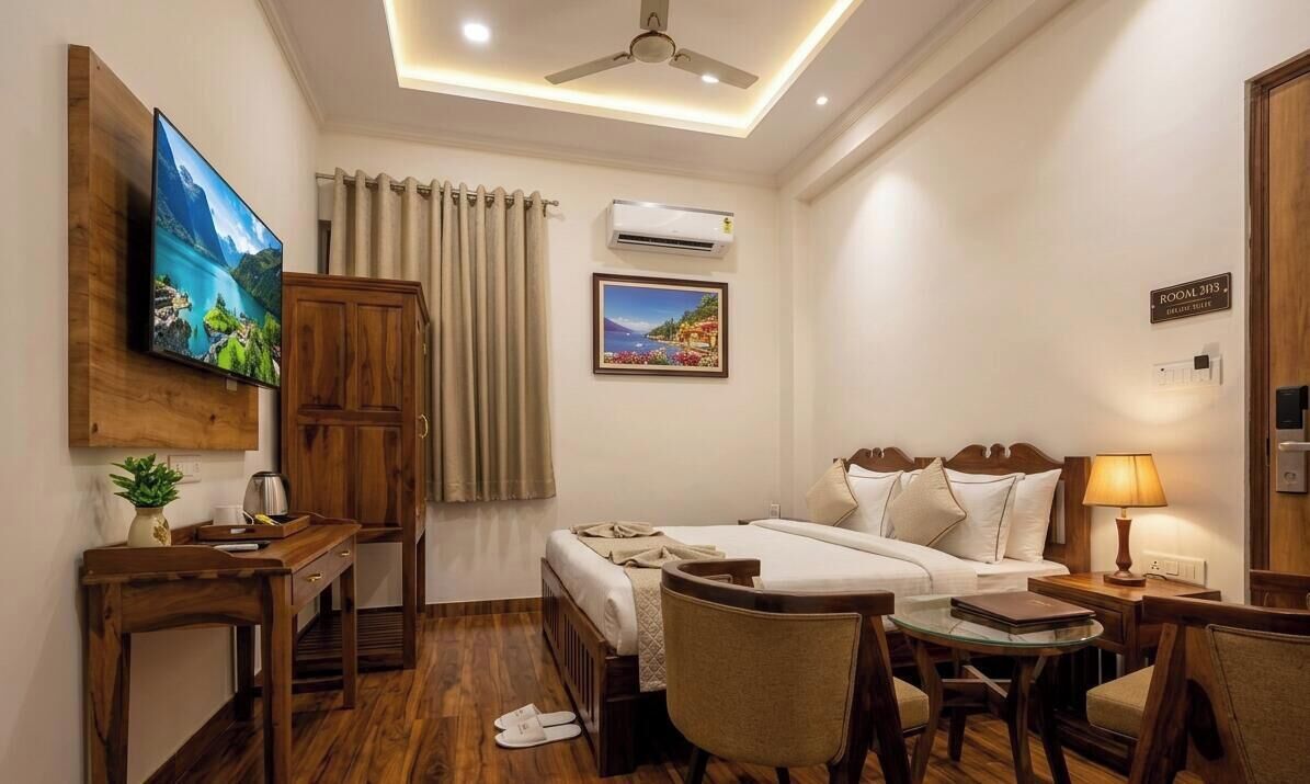 A hotel room with a bed, a desk, a chair, a TV, an air conditioning unit, and a painting on the wall.