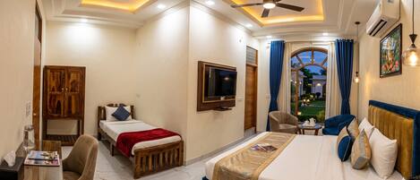 A hotel room with a bed, a TV, a desk with a chair, a window with curtains, and a ceiling fan.