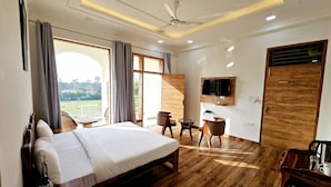 Habitación de hotel con una cama grande, televisión montada en la pared, puerta de madera y vista a un paisaje verde.