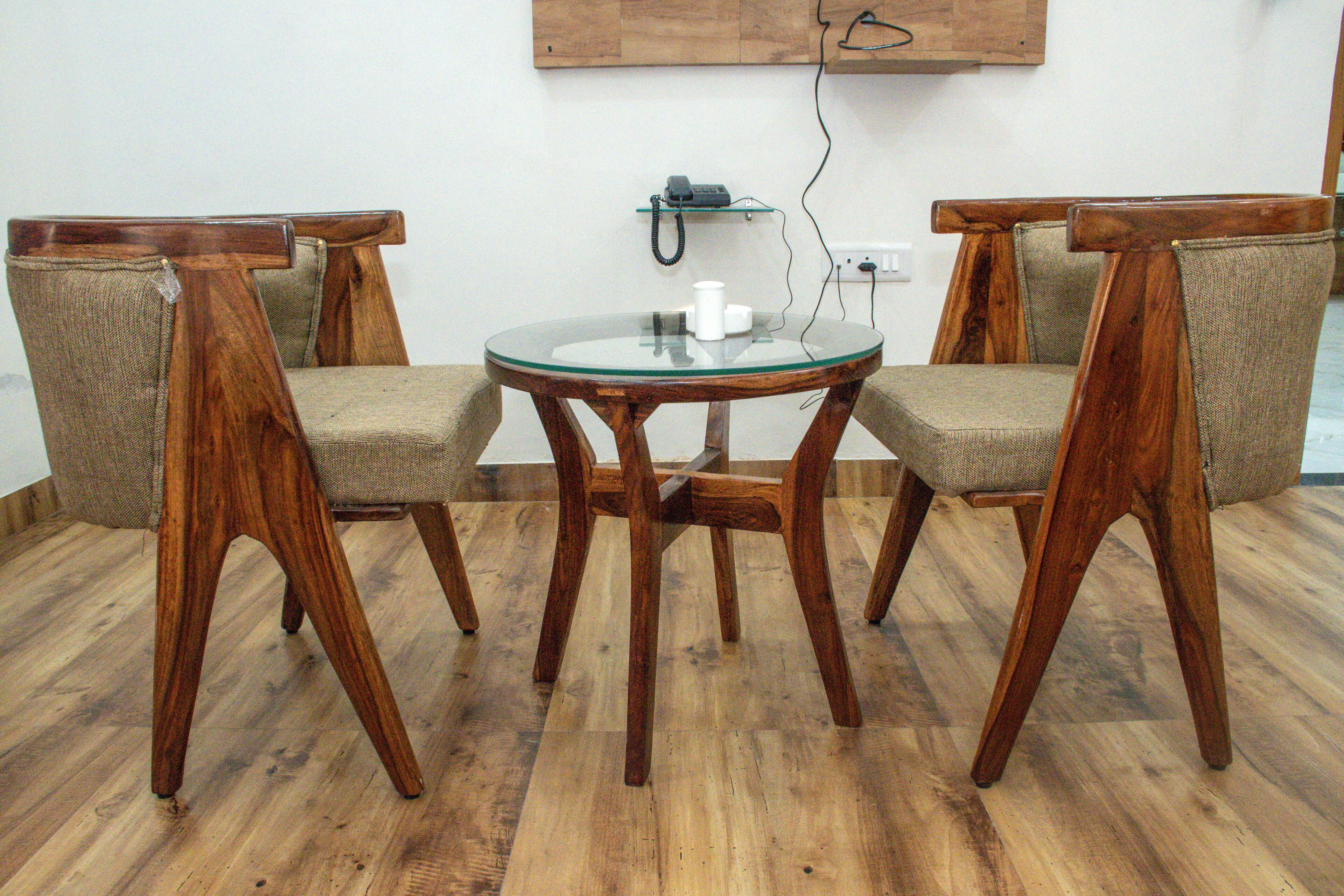 A wooden dining table with four chairs, a glass top, and a telephone on a shelf.