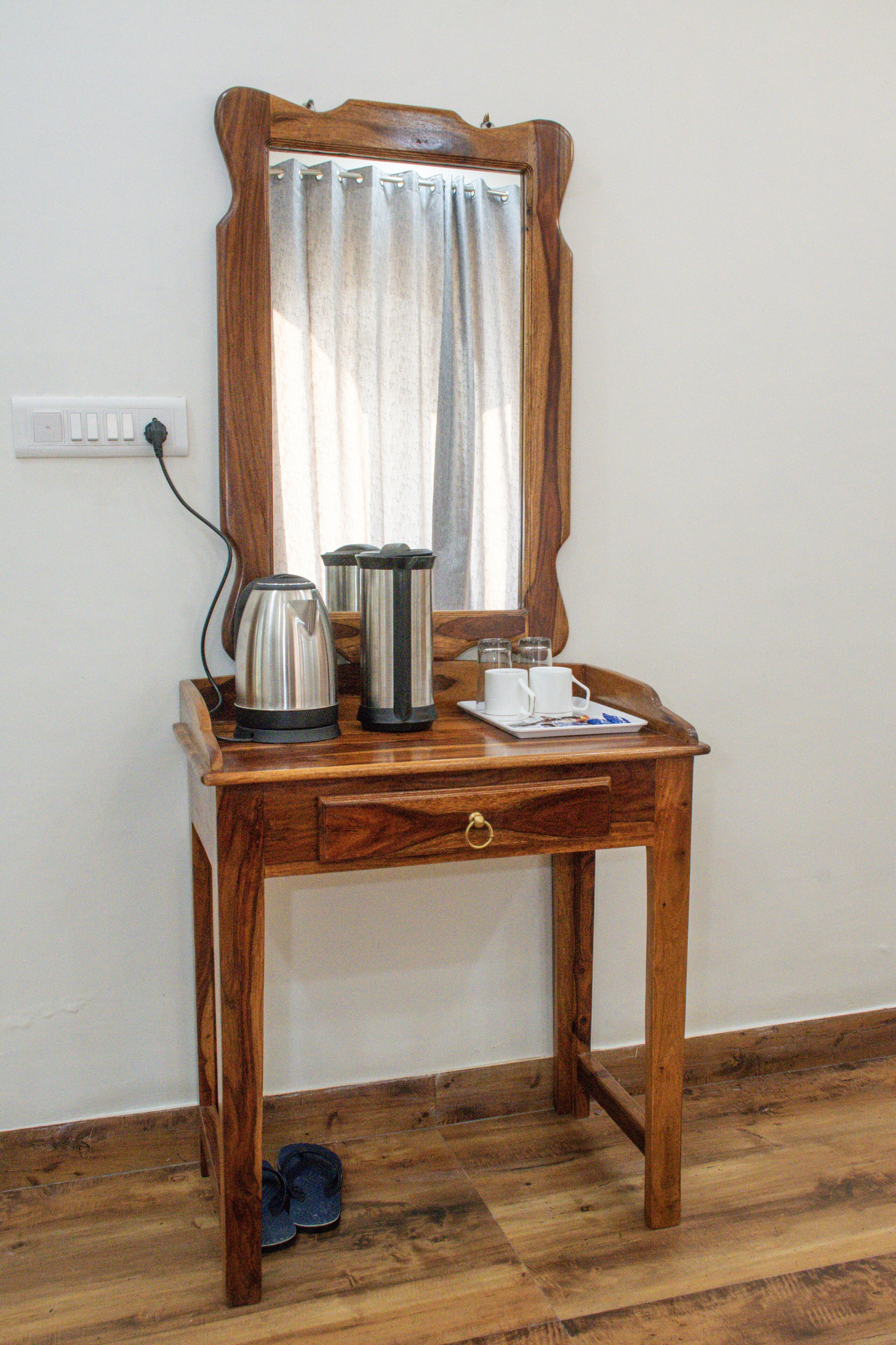 A wooden desk with a mirror, a kettle, a coffee pot, and a tray with cups and saucers.