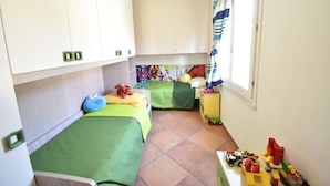 A small, well-lit room with two beds, a window with curtains, a small table with toys, and a colorful wall mural. - APP.LIBECCIO - Appartamento LIBECCIO (Pula)