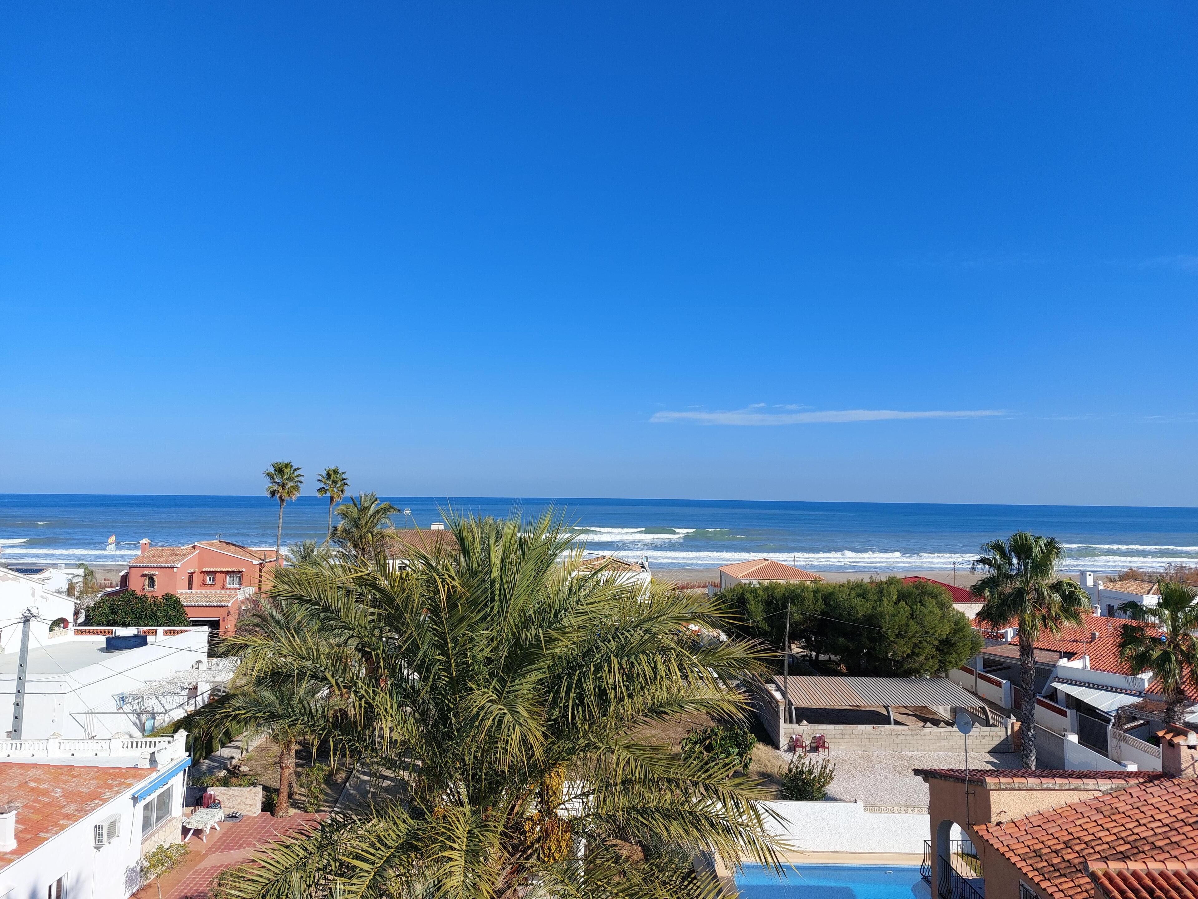 A coastal view with a clear sky, a beach, and residential buildings with a swimming pool.